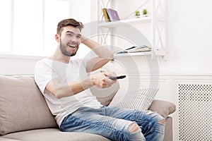 Young man watching tv using remote controller
