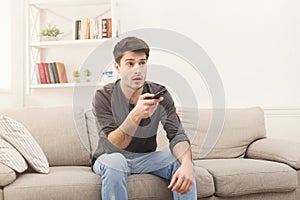 Young man watching tv using remote controller