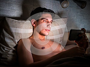 Young man watching a video on cell phone in bed