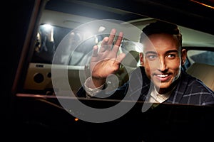 Young man waving from the back of a chauffeur driven limo