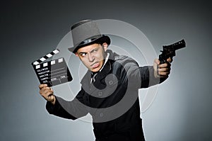 Young man with weapon and clapboard against gray