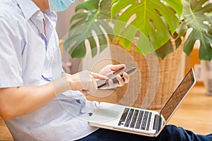 Young man wear mask and studying is working at home with his mobile phone and laptop. Concept of work at home and new technologies