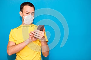 Young man wear medical mask and use mobile phone isolated on blue background