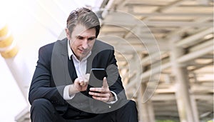 Young man wear suit using smartphone while sitting on city background. Professional businessman reading something on