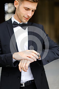 Young man wearing black suit and waiting, loking at watch.