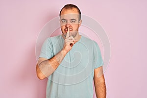 Young man wearing blue casual t-shirt standing over isolated pink background asking to be quiet with finger on lips