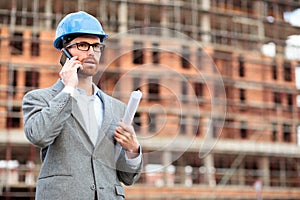 Young man wearing blue hardhat talking on the phone on construction site