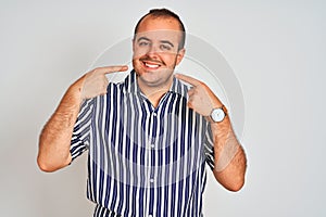 Young man wearing blue striped shirt standing over isolated white background smiling cheerful showing and pointing with fingers