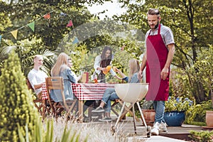 A young man wearing a burgundy apron cooking on a white grill. P