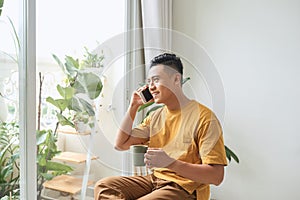 Young man wearing casual clothes talking on a mobile phone in the morning at a window