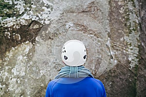 Young man wearing in climbing equipment with rope standing in front of a stone rock