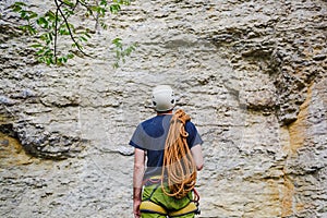 Young man wearing in climbing equipment with rope standing in front of a stone rock