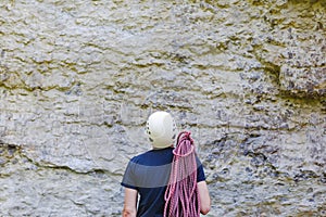 Young man wearing in climbing equipment with rope standing in front of a stone rock