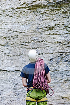 Young man wearing in climbing equipment with rope standing in front of a stone rock
