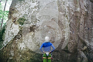 Young man wearing in climbing equipment with rope standing in front of a stone rock and preparing to climb