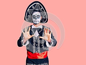 Young man wearing day of the dead costume over background afraid and terrified with fear expression stop gesture with hands,