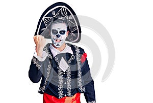 Young man wearing day of the dead costume over background angry and mad raising fist frustrated and furious while shouting with