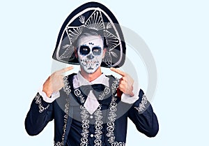 Young man wearing day of the dead costume over background smiling cheerful showing and pointing with fingers teeth and mouth