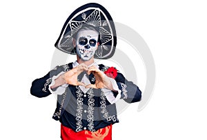 Young man wearing day of the dead costume over background smiling in love doing heart symbol shape with hands