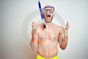 Young man wearing diving snorkel goggles equipent over isolated background crazy and mad shouting and yelling with aggressive