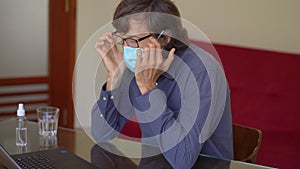 A young man wearing a face mask works from home during coronavirus self-isolation. He is very tired of staying at home