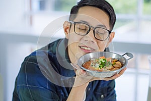 Young man wearing glasses holding the fried egg served on a pan with colorful toppings served on a pan panned egg while sitting