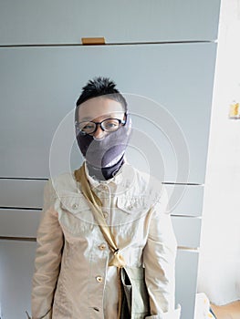A young man wearing glasses and jeans jacket and bag with fabric face mask at home