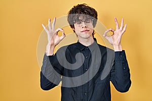 Young man wearing glasses over yellow background relax and smiling with eyes closed doing meditation gesture with fingers
