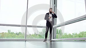 Young man wearing headphones is dancing and shaking his head to the music with large panoramic windows on the background