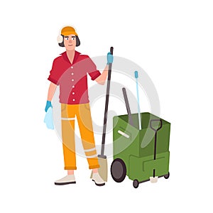 Young man wearing headphones and uniform standing beside mop bucket cart and holding broom. Male cleaning service worker or cleane