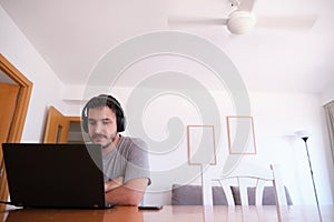 Young man wearing headphones watching series, videos, online classes on a laptop with the fan on