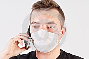 Young man wearing home made cotton face mouth nose virus mask talking on his mobile phone. Studio portrait, white background  -