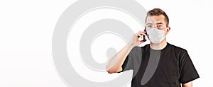 Young man wearing home made cotton face mouth nose virus mask talking on his mobile phone. White background, wide banner  space