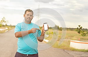Young man wearing jogging dress showing smartphone screen by pointing with hand and finger at park - concept of recommended