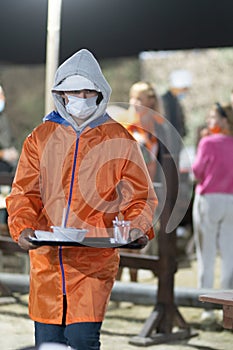 a young man wearing a mask and a protective raincoat as a volunteer during an epidemic and pandemic in a camp to help