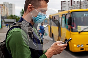 Young man Wearing Medical Mask At Bus Stop Using Smartphone In Ukraine.