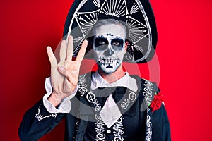 Young man wearing mexican day of the dead costume over red showing and pointing up with fingers number four while smiling