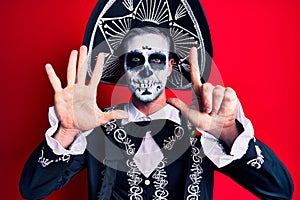 Young man wearing mexican day of the dead costume over red showing and pointing up with fingers number seven while smiling