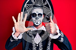 Young man wearing mexican day of the dead costume over red showing and pointing up with fingers number six while smiling confident