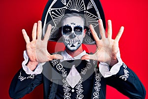 Young man wearing mexican day of the dead costume over red showing and pointing up with fingers number ten while smiling confident