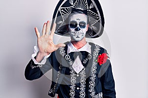 Young man wearing mexican day of the dead costume over white showing and pointing up with fingers number five while smiling