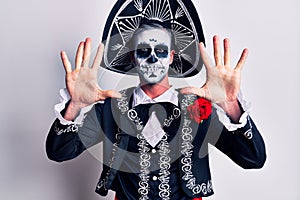 Young man wearing mexican day of the dead costume over white showing and pointing up with fingers number ten while smiling