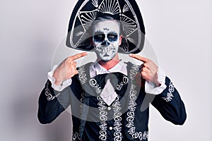 Young man wearing mexican day of the dead costume over white smiling cheerful showing and pointing with fingers teeth and mouth