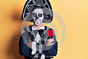 Young man wearing mexican day of the dead costume over yellow happy face smiling with crossed arms looking at the camera