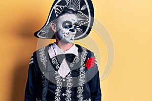 Young man wearing mexican day of the dead costume over yellow looking away to side with smile on face, natural expression