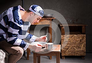 Young man wearing prison uniform eating from aluminum dishes in