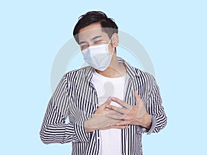 Young man wearing  protective medical mask, feels uncomfortable with his hands on his chest, has difficulty breathing