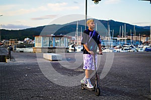 young man wearing purple watching the horizon while carry his electric scooter