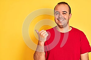 Young man wearing red casual t-shirt standing over isolated yellow background pointing and showing with thumb up to the side with