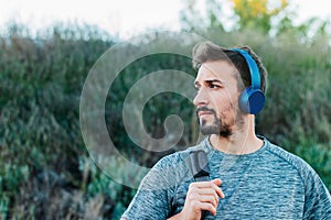 Young man wearing sportswear and bag, walking down the street on his way to the gym, while listening to puss with his blue